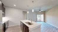 Located in Corinth, TX, this thoughtfully designed one-bedroom, one-bathroom residence offers a well-planned single-level layout with modern finishes throughout. The open-concept living area seamlessly connects the kitchen, dining, and living spaces, all unified by light-toned wood-style flooring. A ceiling fan overhead and a sliding glass door leading to a private patio allow for natural light and easy outdoor access.

The kitchen is a standout feature, anchored by a central island with a white quartz countertop and an undermount stainless steel sink, illuminated by stylish pendant lights. Rich, dark-espresso cabinetry extends to the ceiling, providing ample storage, while stainless steel appliances—including a refrigerator, range, and over-the-range microwave—complete the space.

The bedroom offers plush carpet flooring, a ceiling fan with light, and a window allowing in natural light. It connects conveniently to the hallway, closet, and bathroom. The bathroom features dark cabinetry with a white countertop vanity, a full tub-shower combination with tiled surround, and wood-style flooring. Additional spaces include a dedicated laundry area, a closet, and a hallway, making this a fully functional and efficiently arranged home.