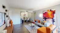 This single-floor residence offers a thoughtfully designed layout that balances open communal spaces with comfortable private quarters. The living room serves as the heart of the home, featuring wood-style flooring, a textured ceiling, and a sliding glass door that invites natural light and provides access to the outdoors. A dedicated dining area sits adjacent to the living space, accented by crown molding and vibrant wall art, creating an intimate setting for meals and entertaining. The galley-style kitchen is outfitted with dark gray cabinetry, black appliances, white subway tile backsplash, and ample counter space along both sides, offering an efficient and functional cooking environment. Two well-sized bedrooms feature plush carpeting and natural light from windows with outdoor views. Each bedroom is served by its own full bathroom, both finished with gray vanity cabinetry, white countertops, a tub-shower combination, and wood-style flooring. A dedicated in-unit laundry closet houses a full-sized washer and dryer, adding everyday convenience. Throughout the space, neutral gray walls provide a clean, modern backdrop that complements the warm and colorful design accents found in each room.