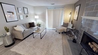 This thoughtfully designed single-floor residence offers a cohesive blend of modern style and practical comfort throughout its well-organized layout. The living room serves as the heart of the home, featuring light-toned walls, wood-style flooring, and a large sliding door dressed with vertical blinds and sheer curtains that allow generous natural light to fill the space. A curated gallery wall, cozy area rug, and warm accent lighting contribute to an inviting, contemporary ambiance.

The kitchen is equipped with dark espresso cabinetry, stainless steel appliances including a refrigerator, range, and over-the-range microwave, complemented by a light quartz countertop and a decorative mosaic tile backsplash. A pantry and in-unit laundry area are conveniently accessible from the kitchen.

The primary bedroom offers a spacious, carpeted retreat with natural light from a window dressed in sheer curtains, featuring a striking rustic wood and metal bed frame as a focal point. A secondary bedroom provides a comfortable, equally well-lit space with soft carpet flooring and coordinated furnishings.

The bathroom includes a dark wood vanity with marble-style countertops and light wood-look flooring. A generously sized walk-in closet with built-in shelving and hanging rods connects directly to the bathroom, offering excellent storage and a seamless layout.