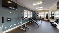 Located at 517 Pink Moon Dr in Rock Hill, South Carolina, this single-floor fitness center is thoughtfully designed to support a wide range of workout routines. The space is defined by its elongated layout, rubber flooring, and a crisp color scheme featuring teal accent walls and cream-toned trim with crown molding details throughout.

The cardio zone, positioned near large glass doors and floor-to-ceiling windows, features treadmills and stationary bikes from Precor, all oriented to take advantage of natural light and views of the outdoor pool area and surrounding community. The open sightlines and abundant fenestration create a bright and motivating atmosphere.

The strength training area is well-equipped with a multi-station cable machine, a full dumbbell rack, adjustable benches, and a power tower for bodyweight exercises. A dedicated boxing station includes a full-size punching bag and an assortment of medicine balls and foam rollers for functional training and recovery. Wall-mounted mirrors along one side of the room enhance the sense of space and allow users to monitor their form during workouts.

Mounted flat-screen televisions are positioned throughout the space for entertainment during exercise sessions. Overhead fluorescent lighting ensures consistent illumination across the entire facility. The overall ambiance is clean, functional, and well-maintained, providing a comprehensive fitness environment for all experience levels.