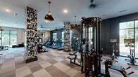 Located at 554 Lancaster Ave in Malvern, PA, this professionally designed fitness center offers a comprehensive, two-zone layout across a single floor. The main gym area features a striking interior aesthetic, with bold dark-blue accent walls, eye-catching graphic-print column wraps, and a checkered rubber tile floor that adds visual depth to the expansive space. Overhead, stylish matte-black pendant lights and ceiling fans provide both ambiance and ventilation. Large windows along the perimeter flood the gym with natural light while offering outdoor views, creating an energizing atmosphere. The equipment lineup is extensive, including a row of treadmills, ellipticals, stationary bikes, a multi-station cable machine, power racks, and a full dumbbell rack, accommodating a wide range of training styles. A separate studio room adjoins the main floor, finished with warm wood-look flooring, floor-to-ceiling mirrors, and large glass doors that open to the outdoors. Illuminated by oversized drum pendant lights and ceiling fans, this open studio is well-suited for yoga, group fitness, or functional training, and is outfitted with medicine balls, resistance bands, BOSU balls, and a wall-mounted equipment rack. Together, the two spaces form a cohesive, well-appointed fitness facility built for performance and comfort.