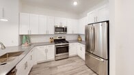 This two-bedroom, two-bathroom residence at Six Points Bloomfield in Bloomfield, NJ, offers a thoughtfully designed single-floor layout with contemporary finishes throughout. The open-concept kitchen is a standout feature, showcasing white shaker cabinetry, subway tile backsplash, gray quartz countertops, and a full suite of stainless steel appliances including a gas range, over-the-range microwave, and French door refrigerator. A spacious island with an undermount sink and pendant lighting provides additional prep space and seating, flowing seamlessly into the living and dining area. The living room is bright and welcoming, benefiting from large windows that invite natural light and offer outdoor views. Wood-look flooring runs throughout, lending a cohesive, modern aesthetic. Both bedrooms are well-proportioned with recessed lighting and windows. The primary bathroom features a double vanity with gray quartz countertops, gold-toned fixtures, and tile flooring, while the second bathroom offers a single vanity with matching finishes and a tub-shower combination. Clean white walls and recessed lighting create a consistent, polished ambiance across all rooms.