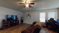This single-story home offers a practical and functional layout with consistent wood-look flooring running throughout every room, creating a cohesive aesthetic. The living area is generously sized, accommodating a large sectional sofa and entertainment setup with ease. Multiple windows along the walls allow natural light to filter in, and a ceiling fan with integrated lighting provides both comfort and illumination. A textured popcorn ceiling is present throughout the home.

The kitchen features white cabinetry with ample upper and lower storage, dark granite-style countertops, and a full suite of white appliances including an electric range, dishwasher, and refrigerator. A window above the sink brings in natural light, enhancing the workspace.

The bathroom is well-appointed with a white vanity, matching dark countertop, and a tub/shower combination. The bedroom is a spacious, neutral room featuring the same wood-look flooring, a ceiling fan with light, and a window dressed with blackout curtains for added privacy. The overall ambiance of the home is casual, practical, and move-in ready.