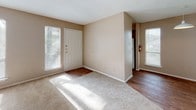 Located at 11600 Huebner Rd in San Antonio, Texas, this single-story unit offers a practical and well-organized layout with a consistent design aesthetic throughout. The living area welcomes natural light through multiple windows fitted with blinds, illuminating the warm beige walls and plush carpeting underfoot. A front entry door flanked by windows creates a bright and inviting entryway that opens into the main living space, where hardwood-style flooring transitions seamlessly from the entry into adjoining areas. The kitchen is efficiently designed with white cabinetry, a white appliance suite including a refrigerator and electric range, light countertops, and a distinctive mosaic tile backsplash that adds a touch of character. Hardwood-style flooring continues through the kitchen for easy maintenance. The bedrooms are generously proportioned, each featuring soft carpeting and natural light from well-placed windows. One bedroom includes a spacious closet with bifold doors. The bathrooms are functional and clean, featuring white vanity cabinetry with light countertops and hardwood-style flooring. Vertical blinds on a sliding door in the living area provide access to an outdoor area, further enhancing the connection to natural light. The overall ambiance is neutral, clean, and move-in ready.