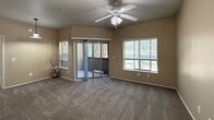 The Lodge presents a well-designed 1-bedroom, 2-bathroom apartment spanning 630 square feet on a single floor. The open kitchen and living area features warm-toned cabinetry, dark granite-style countertops, white appliances including a refrigerator, electric range, microwave, and dishwasher, all set on durable tile flooring. A dedicated in-unit laundry area with a full-size washer and dryer is conveniently accessible from the kitchen. The living room is carpeted and bathed in natural light through multiple windows fitted with blinds, complemented by a ceiling fan and a sliding glass door that opens to a private balcony with tree-lined views. The 140-square-foot bedroom features plush carpet, a ceiling fan, a window with outdoor views, and a mirrored sliding-door closet. The hallway connects to a dedicated closet for additional storage. Both bathrooms are finished with tile flooring and warm cabinetry; the full bathroom includes a double-sink vanity with stone-style countertops and a tub-shower combination. Throughout the unit, neutral beige walls and consistent finishes create a cohesive, comfortable atmosphere well-suited for everyday living.