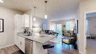 Located at 13040 W Bluemound Rd in Elm Grove, Wisconsin, this well-appointed one-bedroom, one-bathroom residence offers a thoughtfully designed open-concept floor plan. The combined kitchen and living area forms the heart of the home, where rich hardwood-style flooring, neutral tones, and abundant natural light create a welcoming ambiance. The kitchen is outfitted with white shaker cabinetry, granite countertops, a stainless steel refrigerator, dishwasher, and range, along with a peninsula island featuring bar seating — ideal for casual dining. Pendant lighting above the island adds a refined touch. The living room flows naturally from the kitchen and is anchored by large sliding glass doors and windows that bathe the space in daylight and provide direct access to an outdoor area. The bedroom offers a calm retreat with plush carpeting, natural light from a well-positioned window, and comfortable proportions. The bathroom is finished with dark espresso cabinetry, granite countertops, a full vanity with ample storage, and light wood-look tile flooring. Throughout the residence, a cohesive neutral palette and modern finishes contribute to a clean, contemporary aesthetic suited to everyday living.