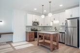 Located on the vibrant Williamson Street corridor in Madison, WI, this thoughtfully designed one-bedroom, one-bathroom unit offers a clean, modern aesthetic across a single floor. Light hardwood flooring flows throughout the entire space, complementing the crisp white walls and creating a bright, cohesive feel.

The combined kitchen and living area serves as the heart of the unit. The kitchen is well-equipped with stainless steel appliances, including a refrigerator, range, microwave, and dishwasher. Two-tone cabinetry — white upper cabinets paired with warm wood lower cabinets — frames a light tile backsplash and white countertops. A freestanding wood kitchen island adds prep space and a natural focal point. Globe pendant lights with brass accents hang overhead, lending a contemporary yet warm ambiance.

The living area features large, black-framed windows that fill the space with natural light and offer views of the surrounding neighborhood. A wall-mounted shelf provides a functional touch.

The bedroom is a serene, light-filled retreat with a broad multi-pane window overlooking mature trees, allowing ample natural light. A dedicated closet offers convenient storage.

The bathroom features warm wood cabinetry, white countertops, a wide vanity mirror, and matte black hardware and fixtures throughout, tying together the unit's modern design language.