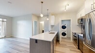 This well-appointed 2-bedroom, 2-bathroom residence offers a thoughtfully designed single-floor layout with modern finishes throughout. The open-concept kitchen and living area serves as the heart of the home, anchored by a sleek kitchen island with a white quartz countertop, an undermount sink, and dark wood cabinetry. The kitchen is equipped with stainless steel appliances — including a refrigerator, range, and microwave — complemented by white upper cabinets, a blue subway tile backsplash, and stylish globe pendant lighting. A dedicated in-unit laundry closet with a stacked washer and dryer adds everyday convenience. The living area features light-toned laminate flooring that extends throughout the unit, with a sliding glass door that opens to a private balcony, allowing natural light to fill the space. The primary bedroom offers a comfortable footprint with multiple windows that invite abundant natural light and include baseboard heating. The second bedroom also features the same consistent flooring and neutral wall tones. A closet with bi-fold doors provides practical storage. Both bathrooms are finished with large-format tile flooring, quartz countertops, and undermount sinks. A wall-mounted mini-split system provides efficient climate control in the living area.