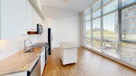 Located in Washington, DC's Southwest Waterfront neighborhood, Unit 315 at 1150 4th St SW is a thoughtfully designed two-bedroom, one-bathroom residence that maximizes its efficient footprint through an open, contemporary layout. The unit features warm hardwood flooring throughout the main living and kitchen areas, transitioning to plush carpeting in both bedrooms.

The kitchen is well-appointed with white cabinetry, granite countertops, a subway tile backsplash, and a full suite of stainless steel appliances, including a side-by-side refrigerator, electric range, built-in microwave, and dishwasher. A mobile kitchen island with a granite top provides additional prep space and flexibility. Ceiling fans and track lighting add practical illumination.

Both bedrooms benefit from floor-to-ceiling windows fitted with horizontal blinds, allowing abundant natural light and views of the surrounding urban landscape and greenery. The elevated ceilings, accented by exposed concrete architectural details, lend the space an airy, modern character.

The bathroom features a granite-topped vanity, a glass-enclosed walk-in shower with white subway tile, and tile flooring. Two closets provide practical storage. The unit's clean, neutral palette and modern finishes create a cohesive and functional living environment.