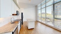 Located in Washington, DC's Southwest Waterfront neighborhood, Unit 315 at 1150 4th St SW is a thoughtfully designed two-bedroom, one-bathroom residence that maximizes its efficient footprint through an open, contemporary layout. The unit features warm hardwood flooring throughout the main living and kitchen areas, transitioning to plush carpeting in both bedrooms.

The kitchen is well-appointed with white cabinetry, granite countertops, a subway tile backsplash, and a full suite of stainless steel appliances, including a side-by-side refrigerator, electric range, built-in microwave, and dishwasher. A mobile kitchen island with a granite top provides additional prep space and flexibility. Ceiling fans and track lighting add practical illumination.

Both bedrooms benefit from floor-to-ceiling windows fitted with horizontal blinds, allowing abundant natural light and views of the surrounding urban landscape and greenery. The elevated ceilings, accented by exposed concrete architectural details, lend the space an airy, modern character.

The bathroom features a granite-topped vanity, a glass-enclosed walk-in shower with white subway tile, and tile flooring. Two closets provide practical storage. The unit's clean, neutral palette and modern finishes create a cohesive and functional living environment.