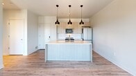 Located on Baum Boulevard in Pittsburgh's vibrant Shadyside neighborhood, this modern 2-bedroom, 1-bathroom unit showcases contemporary design with impressive architectural details throughout. The open-concept kitchen and living area serves as the heart of the home, anchored by a large center island with a crisp white quartz countertop, an undermount sink, and a trio of stylish pendant lights overhead. Light wood cabinetry pairs elegantly with stainless steel appliances, including a range, microwave, and refrigerator. A striking exposed concrete ceiling adds an industrial character to the living space, while large windows flood the area with natural light and offer views of the surrounding Pittsburgh cityscape. The flooring throughout is a light-toned wood-style plank, lending warmth and continuity across the space. Both bedrooms are bright and well-proportioned, with the primary bedroom featuring a floor-to-ceiling window that frames outdoor views. The second bedroom includes a double-door closet and the same concrete ceiling detail. The bathroom is finished to a high standard, with a floating vanity, large mirror, and a glass-enclosed walk-in shower with neutral tile surrounds. A utility room completes the layout, providing practical in-unit functionality.