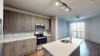 This single-floor unit on 30th Street South in Birmingham, Alabama offers a thoughtfully designed interior with modern finishes and an open, functional layout. The kitchen serves as a central highlight, showcasing wood-toned flat-front cabinetry, quartz countertops, and a full suite of stainless steel appliances including a side-by-side refrigerator with ice maker, electric range, built-in microwave, and dishwasher. A mosaic tile backsplash adds visual texture, while track lighting overhead provides focused illumination. A kitchen island with an integrated single-basin sink and a gooseneck faucet extends the prep and dining space, opening toward a living area with access to an outdoor balcony.

Wood-look flooring runs throughout the main living areas, while the bedrooms feature plush carpeting and ceiling fans for added comfort. One bedroom includes a sliding barn door that opens to a dedicated in-unit laundry area with a stacked washer and dryer. The bathroom is finished with wood-tone vanity cabinetry, a quartz countertop, dark wood-look tile flooring, and a tiled tub-shower combination with a sliding glass door. The overall aesthetic is clean and contemporary throughout.