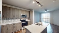 This single-floor unit on 30th Street South in Birmingham, Alabama offers a thoughtfully designed interior with modern finishes and an open, functional layout. The kitchen serves as a central highlight, showcasing wood-toned flat-front cabinetry, quartz countertops, and a full suite of stainless steel appliances including a side-by-side refrigerator with ice maker, electric range, built-in microwave, and dishwasher. A mosaic tile backsplash adds visual texture, while track lighting overhead provides focused illumination. A kitchen island with an integrated single-basin sink and a gooseneck faucet extends the prep and dining space, opening toward a living area with access to an outdoor balcony.

Wood-look flooring runs throughout the main living areas, while the bedrooms feature plush carpeting and ceiling fans for added comfort. One bedroom includes a sliding barn door that opens to a dedicated in-unit laundry area with a stacked washer and dryer. The bathroom is finished with wood-tone vanity cabinetry, a quartz countertop, dark wood-look tile flooring, and a tiled tub-shower combination with a sliding glass door. The overall aesthetic is clean and contemporary throughout.