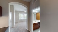 This well-appointed two-bedroom, two-bathroom single-floor residence in Houston, Texas offers a thoughtfully designed layout with generous living space. The open-concept kitchen is a standout feature, showcasing rich cherry wood cabinetry extending to the ceiling, dark granite countertops, a tile backsplash, hardwood flooring, and a central island that flows seamlessly into the dining and living areas. Black appliances, including a refrigerator, range, and built-in microwave, complete the kitchen. Elegant arched doorways connect the living spaces, adding architectural character throughout. The carpeted living and bedroom areas are bright and comfortable, each bedroom featuring a ceiling fan and natural light through large windows with blinds. The primary suite includes a spacious en-suite bathroom with dual sinks, a soaking tub, a large mirror, and access to a walk-in closet. The second bathroom offers a single vanity with cherry cabinetry and a large mirror. A dedicated built-in desk nook provides a practical workspace. An in-unit laundry area with a full-size washer and dryer adds everyday convenience. Neutral tones and consistent finishes throughout create a cohesive and inviting atmosphere.