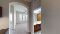 This well-appointed two-bedroom, two-bathroom single-floor residence in Houston, Texas offers a thoughtfully designed layout with generous living space. The open-concept kitchen is a standout feature, showcasing rich cherry wood cabinetry extending to the ceiling, dark granite countertops, a tile backsplash, hardwood flooring, and a central island that flows seamlessly into the dining and living areas. Black appliances, including a refrigerator, range, and built-in microwave, complete the kitchen. Elegant arched doorways connect the living spaces, adding architectural character throughout. The carpeted living and bedroom areas are bright and comfortable, each bedroom featuring a ceiling fan and natural light through large windows with blinds. The primary suite includes a spacious en-suite bathroom with dual sinks, a soaking tub, a large mirror, and access to a walk-in closet. The second bathroom offers a single vanity with cherry cabinetry and a large mirror. A dedicated built-in desk nook provides a practical workspace. An in-unit laundry area with a full-size washer and dryer adds everyday convenience. Neutral tones and consistent finishes throughout create a cohesive and inviting atmosphere.