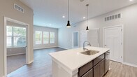 Located at 1 Mossy Grove Ln in Delaware, Ohio, this single-story, 2-bedroom, 2-bathroom home offers a thoughtfully designed open-concept layout with modern finishes throughout. The living room is a standout space, boasting elevated ceilings, light wood-look luxury vinyl plank flooring, and a trio of large windows that flood the room with natural light and offer views of the surrounding greenery. A private exterior door adds convenient access directly from the living area.

The kitchen is a functional centerpiece of the home, featuring dark cabinetry contrasted by crisp white quartz countertops, stainless steel appliances including a refrigerator, range, and microwave, and a large central island with a built-in sink and pendant lighting overhead.

Both bedrooms are carpeted for comfort and include natural light from well-placed windows. The primary bedroom connects to a spacious en-suite bathroom equipped with a double-sink vanity, dark wood cabinetry, a glass-enclosed walk-in shower, and direct access to a walk-in closet with wire shelving. The second bathroom mirrors the modern aesthetic with a single-sink vanity and clean, neutral finishes. Two dedicated closets provide ample storage throughout the home.