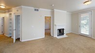 The Lee is a single-floor, two-bedroom, two-bathroom residence designed with a practical and cohesive layout. The living area is anchored by a white-mantled fireplace framed by crown molding, adding a traditional architectural detail to the neutral-toned, carpeted space. Crown molding continues into the dining area, which benefits from natural light through blinded windows and is accented by a chandelier overhead.

The kitchen features white cabinetry paired with dark granite-style countertops, wood-look flooring, and white appliances including a range, microwave, and refrigerator. A peninsula with matching countertop extends into the living space, providing additional prep and serving area. Open shelving within the kitchen adds functional display space.

Both bedrooms are carpeted and fitted with ceiling fans and windows that allow natural light. One bedroom includes built-in shelving along the wall, offering convenient storage. Each bedroom has access to a bathroom, both of which share a consistent design: white tile flooring with black accent insets, dark countertops, white cabinetry, and a shower-tub combination with a black tile border accent.