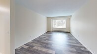Located at 500 W Genesee St in Chittenango, NY, this one-bedroom, one-bathroom unit offers a practical and comfortable single-floor layout. The living room is a generously proportioned space finished with durable hardwood-style plank flooring and neutral cream-toned walls. A large picture window floods the room with natural light while offering views of the surrounding greenery, and a baseboard heating system runs along the perimeter for year-round comfort. The layout opens into a secondary area with hardwood-style flooring that connects seamlessly to the kitchen. The kitchen is well-equipped with crisp white cabinetry, granite-style countertops, and a full suite of white appliances including a refrigerator, electric range, and dishwasher. A double-basin sink and under-cabinet range hood complete the functional setup. The bedroom features plush carpeting, a wide sliding closet for storage, and a window that brings in natural light. The full bathroom includes a soaking tub and shower combination, a white vanity with granite-style countertop, a medicine cabinet mirror, and tile flooring. Throughout the unit, the clean, neutral palette and consistent finishes create a cohesive and move-in-ready living environment.