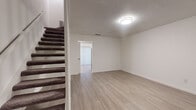 This two-story residence offers a clean, functional layout designed with practical living in mind. The main level features light wood-style laminate flooring that flows through the open living area, creating a bright and cohesive feel. A carpeted staircase with dark treads connects the two floors, adding a subtle contrast to the light interior palette. The kitchen is well-appointed with stainless steel appliances, including a range, microwave, and dishwasher, complemented by gray cabinetry, a tiled backsplash, and a large vertical blind-covered sliding door that fills the space with natural light. Ceilings throughout feature a textured finish, adding dimension to the otherwise crisp white walls and clean white baseboards. Upstairs, the bedrooms are carpeted for comfort and equipped with ceiling fans. Each bedroom features a neutral color palette with ample wall space and windows dressed with blinds for light control. The bathroom includes a full tub-and-shower combination with white tile surround, a curved shower rod, sleek brushed nickel fixtures, and a towel bar — all set above light wood-style flooring. The overall ambiance is understated and move-in ready, offering a versatile canvas for any living style.