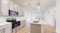 This well-appointed 1-bedroom, 1-bathroom unit in Enola, PA offers a thoughtfully designed layout that maximizes comfort and functionality. The open-concept kitchen and living area serves as the heart of the home, where light-toned luxury vinyl plank flooring, recessed lighting, and a neutral color palette create a bright, modern atmosphere. The kitchen is a standout feature, equipped with grey shaker-style cabinetry, crisp white countertops, a large center island with a stainless steel double sink and elegant pendant lighting above, and a full suite of stainless steel appliances including a refrigerator, electric range with over-the-range microwave, and dishwasher. The living area flows seamlessly from the kitchen and is bathed in natural light from a sliding glass door that opens to an outdoor view. The generously sized bedroom features plush carpeting and multiple windows that bring in ample natural light. A dedicated walk-in closet outfitted with wire shelving provides practical storage. The bathroom mirrors the home's cohesive design with matching grey cabinetry, a white countertop vanity, and hardwood-style flooring. Clean lines, modern finishes, and a bright, open feel define this move-in-ready unit.