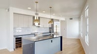 Located at 2188 Highland Drive in Salt Lake City, UT, this modern 2-bedroom, 2-bathroom residence showcases a thoughtfully designed open-concept floor plan with clean lines and upscale finishes throughout. Light hardwood flooring flows seamlessly across the entire living space, enhancing the bright, airy atmosphere created by abundant natural light from large windows.

The heart of the home is a stunning chef's kitchen featuring crisp white upper cabinetry, a bold dark-topped island with a navy blue base, a marble-style backsplash, stainless steel appliances, a wine refrigerator, and striking brushed gold pendant lights and hardware. The kitchen opens directly into the combined dining and living area, which benefits from a wall of windows offering views of the surrounding neighborhood.

Both bedrooms are generously sized, calm, and filled with natural light, complemented by ample closet space. The primary bedroom offers a comfortable retreat with room for a full suite of furnishings. The two bathrooms are finished in a contemporary style, featuring gray vanity cabinetry with gold hardware, a walk-in glass shower, and wood-look flooring. Additional conveniences include in-unit laundry, four closets, a hallway, and a private balcony.