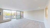 Located at 5 Stonehill Dr, Unit 4F in Stoneham, MA, this one-bedroom, one-bathroom residence offers a well-organized layout across a single floor. The spacious living area is a standout feature, showcasing large floor-to-ceiling sliding glass doors that open onto a private balcony, flooding the room with natural light and providing open views of the surrounding neighborhood. Soft neutral carpeting and clean white baseboard heating run throughout the living and bedroom areas, creating a cohesive and comfortable feel. The kitchen is bright and modern, outfitted with crisp white shaker-style cabinetry, light countertops, stainless steel appliances including a refrigerator, range, microwave, and dishwasher, and light wood-look flooring that adds warmth to the space. The generously sized bedroom features recessed lighting, a wall-mounted AC unit, a large window with tree-lined views, and plush carpeting. The bathroom is finished in clean white tile, complete with a tub-shower combination accented by a decorative mosaic tile border, a vanity with ample storage, and tile flooring. Two hallways and a dedicated closet provide practical storage and smooth circulation throughout this well-appointed Stoneham residence.
