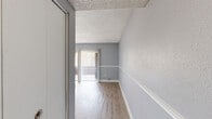 Located at 6919 Bonair Drive in Tampa, Florida, this two-bedroom, one-bathroom single-floor home offers a functional and well-organized layout with a clean, neutral aesthetic throughout. The interior is finished with cool gray walls accented by white trim, creating a cohesive and modern feel. The living area features wood-look laminate flooring and leads directly to a balcony through a sliding glass door dressed with vertical blinds, allowing ample natural light to fill the space. An arched window in the dining area adds a distinctive architectural touch, complemented by a hanging pendant light. The kitchen is outfitted with white cabinetry, a granite-style countertop, tile backsplash, tile flooring, and white appliances including a range and refrigerator. Both bedrooms are carpeted and feature textured ceilings, with the primary bedroom offering a dedicated closet and an additional walk-in closet area. The second bedroom includes a bi-fold closet. The bathroom is equipped with a tub-shower combination, a white vanity with granite-style countertop, and wood-look tile flooring. A hallway and entrance complete the efficient floor plan of this Tampa residence.