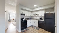 This two-floor home offers a thoughtfully designed layout that balances functionality with modern style throughout. The living room serves as the heart of the main floor, featuring warm wood-look flooring, a striking sputnik chandelier, and decorative wall sconces that lend an eclectic yet cohesive character to the space. A plush area rug anchors the seating area, which flows naturally toward the entryway, where a light-filled door provides a welcoming sense of openness.

The kitchen is a standout feature, showcasing crisp white shaker cabinetry, classic subway tile backsplash, granite-look countertops, and a full suite of black appliances including a range, dishwasher, and refrigerator. The adjacent dining area is bright and intimate, with natural light filtering through shuttered windows and stylish sunburst wall mirrors adding a decorative accent.

A half bathroom on the main floor is finished with a white vanity, matte black fixtures, and a frameless mirror, maintaining the home's clean, contemporary aesthetic. The upper level includes a carpeted bedroom currently configured as a home office, offering a quiet and versatile space with ample room and natural light. The dollhouse view reveals a well-organized floor plan that maximizes usable space across both levels, making this home both practical and visually appealing.