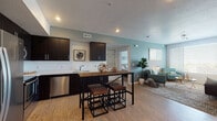 This single-floor residence is designed with a modern aesthetic, combining functional layout with contemporary finishes throughout. The open-concept kitchen is a standout feature, outfitted with dark espresso cabinetry extending to the ceiling, white countertops, and a full suite of stainless steel appliances including a French door refrigerator, electric range, built-in microwave, and dishwasher. Light wood-style flooring runs through the kitchen and into the adjoining dining area, where a wood-top bar-height table with industrial-style metal stools serves as a central gathering point.

The living room offers generous natural light through large windows with horizontal blinds, providing elevated outdoor views. The space is accented by soft blue-grey walls and a textured ceiling, creating a relaxed yet polished ambiance.

Two bedrooms are carpeted for comfort, each featuring windows that bring in natural light and ceiling fans for ventilation. The soft color palette carries through both rooms, lending a calm, cohesive feel.

Two full bathrooms include dark vanity cabinetry with white countertops, large-format tile flooring, and tub-shower combinations. One bathroom offers an elongated layout with a walk-in closet nearby, adding practical storage to the space.