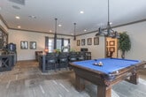 This single-floor community space in Lawrenceville, GA, offers a thoughtfully designed layout that balances leisure, socializing, and functionality. The interior showcases a cohesive rustic-modern aesthetic, defined by warm wood-toned flooring, crown molding with contrasting dark trim, neutral walls, and recessed lighting throughout.

The game room is a standout feature, centered around a full-size pool table with a vibrant blue felt surface, illuminated by industrial-style pendant lighting. Natural light filters in through grommet-panel curtained windows, and a wall-mounted television adds entertainment options alongside a mounted cue rack.

Adjacent to the game room, a lounge area provides a relaxed retreat with rich leather armchairs, framed wall art, and a coffee bar station. A dedicated dining space features a marble-topped table beneath a wrought-iron chandelier, surrounded by upholstered seating and draped windows that invite natural light.

A private nook functions as a business center, equipped with desktop computers on a rustic wood desk, bar-height seating, and framed artwork above. A secondary seating area with a wooden credenza and decorative accents connects the zones via a glass-paned interior door, contributing to the space's open yet defined flow.
