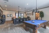 This single-floor community space in Lawrenceville, GA, offers a thoughtfully designed layout that balances leisure, socializing, and functionality. The interior showcases a cohesive rustic-modern aesthetic, defined by warm wood-toned flooring, crown molding with contrasting dark trim, neutral walls, and recessed lighting throughout.

The game room is a standout feature, centered around a full-size pool table with a vibrant blue felt surface, illuminated by industrial-style pendant lighting. Natural light filters in through grommet-panel curtained windows, and a wall-mounted television adds entertainment options alongside a mounted cue rack.

Adjacent to the game room, a lounge area provides a relaxed retreat with rich leather armchairs, framed wall art, and a coffee bar station. A dedicated dining space features a marble-topped table beneath a wrought-iron chandelier, surrounded by upholstered seating and draped windows that invite natural light.

A private nook functions as a business center, equipped with desktop computers on a rustic wood desk, bar-height seating, and framed artwork above. A secondary seating area with a wooden credenza and decorative accents connects the zones via a glass-paned interior door, contributing to the space's open yet defined flow.