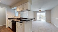This single-floor, 2-bedroom, 2-bathroom residence offers a well-organized layout designed for comfortable everyday living. The kitchen serves as a focal point, featuring white shaker-style cabinetry with brushed gold hardware, dark granite countertops, and a full suite of black appliances including a range, microwave, dishwasher, and refrigerator. A peninsula with an extended counter provides additional workspace and separates the kitchen from the adjacent dining area, which is illuminated by a pendant light fixture overhead. Wood-look flooring runs throughout the kitchen and dining areas, adding warmth and visual continuity.

The living area transitions to soft carpeting and is brightened by a ceiling fan with integrated lighting and a sliding glass door that opens to an outdoor balcony, allowing natural light to fill the space. Each bedroom continues the carpeted flooring and includes a ceiling fan, with windows fitted with blinds for light control and privacy.

The bathrooms feature the same white cabinetry with granite countertops, wood-look flooring, and tiled shower-tub surrounds. A hallway provides access between the bedrooms and bathrooms, with closet storage visible nearby. The overall aesthetic is clean and cohesive throughout.