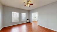 Located at 117 S Isabel St in Glendale, California, this ground-floor unit offers a practical and efficiently organized layout comprising a living room, kitchen, closet, and bathroom. The living room serves as the central space of the unit, finished with warm wood-look flooring that extends throughout. Gray-painted walls provide a neutral backdrop, while a ceiling fan with integrated lighting overhead offers both air circulation and illumination. Two windows fitted with horizontal blinds allow natural light to filter into the room, contributing to an open and airy feel. A wall-mounted heater provides supplemental climate control.

The kitchen is configured in a galley style, featuring white cabinetry above and below the countertops, a stainless steel sink, and white appliances including a gas range and refrigerator. A window above the sink brings in additional natural light. Glass-front cabinet displays add a classic touch to the kitchen's clean, all-white aesthetic.

The bathroom is finished with light tile flooring and white walls, housing a tub-shower combination, a single-sink vanity, and a window that provides ventilation and natural light. The unit also includes a dedicated closet for storage, rounding out this compact yet functional space.