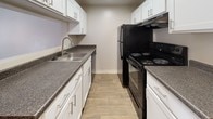 This single-floor unit offers a well-organized layout designed for comfortable, everyday living. The living area greets you with rich, dark wood-style flooring and an abundance of natural light streaming through slatted blinds on both a glass-paned door and an adjacent window, creating a bright and welcoming atmosphere. Neutral beige walls throughout lend a clean, cohesive look to the entire space.

The galley-style kitchen is thoughtfully designed with white cabinetry lining both sides, dark speckled countertops, a stainless steel sink, and black appliances including a range with overhead ventilation and a full-size refrigerator. Light wood-tone flooring runs through the kitchen, complementing the crisp white cabinets.

A dedicated dining area adjacent to the kitchen features warm wood-style flooring and an overhead pendant light fixture, providing a defined space for meals. The bedroom is carpeted for comfort, includes a window with outdoor views, and is equipped with a sliding-door closet offering ample storage.

The bathroom presents a clean and functional design with white cabinetry, dark speckled countertops consistent with the kitchen, an integrated sink with brushed nickel fixtures, and a mirrored medicine cabinet above the vanity. Overall, the space delivers a modern, move-in-ready feel with consistent finishes throughout.