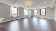 This single-floor residence offers a thoughtfully designed open-concept layout finished with rich, dark hardwood flooring throughout. The expansive living area is anchored by a sleek fireplace and a chandelier overhead, with multiple large black-framed windows framing sweeping panoramic views of the city skyline and waterfront beyond. Natural light flows generously across the space, enhancing its airy, contemporary feel.

The kitchen is well-appointed with dark espresso cabinetry extending to the ceiling, white quartz countertops, a textured tile backsplash, and a full suite of stainless steel appliances including a gas range, built-in microwave, and French door refrigerator. A breakfast bar island provides additional prep and seating space, seamlessly connecting the kitchen to the living area.

The bedrooms are generously sized, each featuring hardwood floors, neutral warm-toned walls, and windows with elevated city or water views. A hallway connects the private rooms efficiently to the rest of the unit.

The bathroom features large-format tile flooring, a soaking tub with a decorative mosaic tile surround, and a window offering remarkable elevated views. Throughout the unit, clean lines, neutral tones, and quality finishes define a cohesive and polished modern aesthetic.