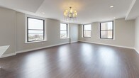 This single-floor residence offers a thoughtfully designed open-concept layout finished with rich, dark hardwood flooring throughout. The expansive living area is anchored by a sleek fireplace and a chandelier overhead, with multiple large black-framed windows framing sweeping panoramic views of the city skyline and waterfront beyond. Natural light flows generously across the space, enhancing its airy, contemporary feel.

The kitchen is well-appointed with dark espresso cabinetry extending to the ceiling, white quartz countertops, a textured tile backsplash, and a full suite of stainless steel appliances including a gas range, built-in microwave, and French door refrigerator. A breakfast bar island provides additional prep and seating space, seamlessly connecting the kitchen to the living area.

The bedrooms are generously sized, each featuring hardwood floors, neutral warm-toned walls, and windows with elevated city or water views. A hallway connects the private rooms efficiently to the rest of the unit.

The bathroom features large-format tile flooring, a soaking tub with a decorative mosaic tile surround, and a window offering remarkable elevated views. Throughout the unit, clean lines, neutral tones, and quality finishes define a cohesive and polished modern aesthetic.