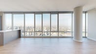 Located in Chicago's River North neighborhood, this two-bedroom, two-bathroom high-rise residence offers sweeping panoramic views of the Chicago skyline through dramatic floor-to-ceiling glass windows that wrap the living areas and bedrooms. Light hardwood flooring flows throughout the open-concept layout, complementing the clean, contemporary aesthetic. The combined living, dining, and kitchen area serves as the heart of the home, anchored by a structural column that adds an architectural focal point. The modern kitchen is equipped with stainless steel appliances including a gas range, dishwasher, and French door refrigerator, paired with two-tone cabinetry in muted gray tones and a white subway tile backsplash. Both bedrooms benefit from the same expansive city views via floor-to-ceiling windows, with the primary bedroom offering direct access to an en-suite bath. The bathrooms are finished with large-format marble-style tile, including a soaking tub with a frameless glass surround. Three closets provide generous storage, and an in-unit laundry area with a stacked washer and dryer adds everyday convenience. Track lighting and roller shades complete the refined, urban aesthetic of this well-appointed residence.
