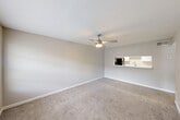 This single-floor residence offers a practical and comfortable layout encompassing a combined kitchen and living room, one bedroom, a closet, and a full bathroom. The living room is a welcoming open space featuring neutral-toned carpet, soft beige walls, white baseboards, and a ceiling fan with integrated lighting. A window with blinds allows natural light to fill the room, creating a bright and airy atmosphere, while a front entry door adds convenience and accessibility. The kitchen is designed in a galley style with wood-look flooring, white upper cabinetry, light speckled countertops, and a full suite of black appliances including a refrigerator, electric range, over-the-range microwave, and ample counter space on both sides. The bedroom is a well-proportioned room finished with the same soft carpet and neutral walls as the living area, equipped with its own ceiling fan, a window with blinds for natural light, and direct access to the closet. The bathroom features a clean, white tiled tub-shower combination with chrome fixtures, complemented by a simple, bright aesthetic. Throughout the space, consistent finishes and a neutral color palette create a cohesive, move-in ready environment.