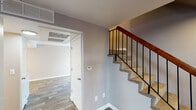 This two-floor residence offers a well-organized layout with a clean, modern aesthetic throughout. The main level features durable wood-style plank flooring that flows through the entry, living areas, and kitchen. The entry area provides a welcoming transition into the home, with neutral gray walls and crisp white baseboards setting a consistent tone across both floors. A sliding glass door in the living area allows natural light to fill the space and provides access to an outdoor area. The kitchen is efficiently designed with ample white cabinetry, light granite-style countertops, and a full suite of black appliances including a range, refrigerator, and dishwasher, all illuminated by a recessed overhead light fixture. A staircase with warm wood handrails and black iron balusters connects the two levels, accented by neutral carpet treads. The upper level houses the bedrooms, each finished with plush carpet, taupe-toned walls, and windows fitted with horizontal blinds that allow for natural light and privacy control. Bedrooms include closets with sliding panel doors, providing practical storage. The overall design is understated and functional, featuring neutral tones and consistent finishes that create a cohesive living environment throughout the home.