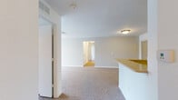 This single-floor residence offers a practical and comfortable layout designed for everyday living. The open-concept living area is anchored by plush wall-to-wall carpeting and connects seamlessly to the kitchen via a peninsula counter, creating an inviting communal space. A sliding door reveals a built-in shelving unit, adding convenient storage directly off the living area.

The galley-style kitchen is outfitted with warm honey-toned wood cabinetry, a dual-basin sink, electric range and oven, a full-size refrigerator, and a dedicated pantry with wire shelving. Durable hardwood-style flooring runs throughout the kitchen, providing a clean contrast to the carpeted living spaces.

A generously sized bedroom features plush carpeting, a ceiling fan with overhead lighting, and a wide window that fills the room with natural light. The hallway connects the main living areas to the private quarters and leads to two full bathrooms, each featuring a tiled shower-tub combination, hardwood-style flooring, and clean white finishes. One bathroom includes a warm wood vanity with ample cabinet storage beneath a white countertop.

The entry foyer offers a welcoming transition into the home, with a carpeted hallway connecting all areas of the floor plan. Textured ceilings, neutral wall tones, and flush-mount lighting fixtures are consistent throughout, lending the space a cohesive and move-in-ready aesthetic.