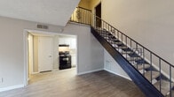Located at 3214 Valley Bluff Dr in Doraville, GA, this two-story residence offers a well-organized layout across two distinct levels. The main floor centers on a spacious living area with light wood-look flooring and a textured ceiling that extends upward to an impressive double-height volume, creating a sense of openness and airiness. A sliding glass door provides direct access to an outdoor balcony, allowing natural light to flow freely into the living space. A decorative wrought-iron staircase with a geometric railing pattern serves as a visual focal point while connecting the two floors, with the upper level overlook visible from below.

The kitchen is a functional galley-style space fitted with white raised-panel cabinetry, light countertops, a stainless sink, and black appliances including a range and refrigerator. A second, more compact bathroom on the main level features a white vanity and wood-look flooring, while an additional bathroom includes a tiled tub and shower surround.

Upstairs, the bedroom features plush carpeting, a distinctive shiplap-style ceiling, and a window that draws in natural light and neighborhood views. A separate open room on this level features dark wood-look flooring and benefits from the soaring ceiling height visible from the staircase landing, offering flexible use as a living, dining, or workspace.