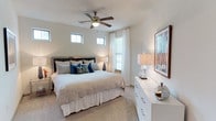 This thoughtfully designed single-floor residence offers a cohesive blend of modern finishes and comfortable living spaces. The kitchen is a standout feature, showcasing rich dark-wood cabinetry, granite countertops, stainless steel appliances including a range, microwave, and refrigerator, and a kitchen island with pendant lighting that adds a warm, inviting glow. A pantry provides additional storage just steps away. The open dining area flows seamlessly from the kitchen and features polished concrete-style flooring that adds a contemporary edge. A glass-top dining table anchors the space alongside an art-lined wall, creating a gallery-like atmosphere. The living room is bathed in natural light from large windows dressed with horizontal blinds and elegant patterned drapes. A ceiling fan overhead, a plush area rug, and a glass coffee table contribute to the room's relaxed yet refined ambiance. A door provides direct access to an exterior space, enhancing connectivity to the outdoors. The bedroom continues the theme of comfort and style, with soft carpeting, multiple windows that invite natural light, a ceiling fan, and ample room for generous furnishings. The neutral palette throughout the residence creates a calm, welcoming environment that is both functional and visually appealing.