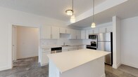 This single-floor unit presents a cohesive, modern design defined by a crisp white palette and clean finishes throughout. The kitchen serves as a functional centerpiece, outfitted with full stainless steel appliances including a refrigerator, range, microwave, and dishwasher. White flat-panel cabinetry with brushed nickel hardware lines the walls, complemented by a white quartz countertop, tile backsplash, and a central island that provides additional prep and gathering space. Pendant lighting overhead adds a polished touch. The flooring in the kitchen and main living areas features a polished concrete finish, lending an industrial-modern aesthetic.

The bedrooms are carpeted for comfort and receive natural light through large windows fitted with horizontal blinds. Ceiling fans with integrated light fixtures are present in select bedrooms. A generously sized walk-in closet with dual shelving rods and carpet flooring provides substantial storage.

The bathrooms are finished in a clean, all-white style. One bathroom features a full tub-shower combination with tile surround, while another includes a wide vanity with white quartz countertop, an under-mount sink, and a large mirror. Concrete flooring extends through the bathrooms, reinforcing the unit's consistent modern character throughout.