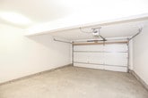 This single-level garage offers a clean, open layout designed for practical use. The space is finished with smooth white-painted walls throughout, lending a bright and well-maintained appearance. The concrete floor spans the entire area, providing a durable and easy-to-maintain surface well suited for vehicle parking, storage, or workshop activities.

A motorized overhead garage door with an automatic opener is installed at the front, offering convenient access. The door itself features a classic raised-panel design with metal hardware and is supported by a standard rail-and-arm drive system mounted to the ceiling. Interior access is provided through a paneled white entry door, which connects directly to the main living space — a practical feature for everyday use.

The garage includes an electrical panel conveniently located near the interior entry point, along with multiple electrical outlets and light switches positioned throughout. Overhead lighting is installed in the ceiling, ensuring the space remains well-lit. A structural beam runs across the ceiling, adding to the overall integrity of the build.

The clean, uncluttered design of this garage makes it highly versatile — whether used for vehicle storage, a hobby workspace, or additional utility storage, this space is ready to accommodate a variety of needs.