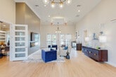 Located at 1285 J D Miller Rd in Santa Rosa Beach, Florida, this single-story community clubhouse offers a well-appointed gathering space designed with a modern coastal aesthetic. The entryway greets visitors with soaring ceilings, light wood-look flooring in a herringbone pattern, and a striking brass-and-glass chandelier, establishing an elegant tone throughout.

The main lounge area features towering ceilings, a wall-mounted flat-screen TV above a linear fireplace, and a seating arrangement of plush cream sofas and bold navy velvet accent chairs atop a layered area rug. Multiple glass-paned French doors allow abundant natural light and provide views of the outdoor pool area. A secondary lounge space includes additional casual seating and a full kitchen with dark cabinetry, stainless steel appliances, a breakfast bar with pendant lighting, and direct outdoor access.

A dedicated dining room accommodates a large oval wood table beneath an industrial-style cage chandelier. A quiet corridor leads to private office or meeting spaces with glass-panel doors. The fitness center is generously sized, equipped with treadmills, ellipticals, cycling machines, and free weights, illuminated by natural light from surrounding windows and ceiling fans overhead.