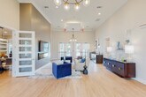 Located at 1285 J D Miller Rd in Santa Rosa Beach, Florida, this single-story community clubhouse offers a well-appointed gathering space designed with a modern coastal aesthetic. The entryway greets visitors with soaring ceilings, light wood-look flooring in a herringbone pattern, and a striking brass-and-glass chandelier, establishing an elegant tone throughout.

The main lounge area features towering ceilings, a wall-mounted flat-screen TV above a linear fireplace, and a seating arrangement of plush cream sofas and bold navy velvet accent chairs atop a layered area rug. Multiple glass-paned French doors allow abundant natural light and provide views of the outdoor pool area. A secondary lounge space includes additional casual seating and a full kitchen with dark cabinetry, stainless steel appliances, a breakfast bar with pendant lighting, and direct outdoor access.

A dedicated dining room accommodates a large oval wood table beneath an industrial-style cage chandelier. A quiet corridor leads to private office or meeting spaces with glass-panel doors. The fitness center is generously sized, equipped with treadmills, ellipticals, cycling machines, and free weights, illuminated by natural light from surrounding windows and ceiling fans overhead.