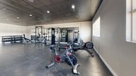 Located at 1601 N Oracle Rd in Tucson, Arizona, this fitness center offers a generously sized, single-floor exercise facility designed to accommodate a wide variety of workout needs. The space features a durable dark concrete-style flooring throughout, complemented by a drop-panel ceiling with recessed lighting that creates a clean, functional atmosphere.

The cardio section is well-appointed with treadmills, elliptical machines, a stationary bike, and a rowing machine, all positioned beneath wall-mounted flat-screen televisions for entertainment during workouts. Natural light filters in through multiple windows along the walls, adding brightness to the space.

The strength training area includes a multi-station cable machine, a squat/power rack, and a full rack of dumbbells ranging across various weights, providing options for both beginner and advanced lifters. Large mirrors line portions of the walls, enhancing the sense of space and allowing users to monitor their form.

A dedicated open-floor zone offers ample room for functional fitness, stretching, and group exercises, stocked with stability balls, medicine balls, and additional accessories on organized racks. A water fountain is conveniently located within the facility. The overall layout is thoughtfully arranged to ensure smooth traffic flow, making this fitness center a comprehensive and practical space for all levels of fitness enthusiasts.