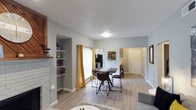 Located in Dallas, this single-floor residence offers a warm and welcoming interior designed for comfortable everyday living. The open-concept layout connects the living, dining, and kitchen areas seamlessly, creating a spacious and functional flow throughout the main living space.

The living area features a classic brick fireplace with a rustic wood mantle, complemented by built-in shelving that provides both storage and display space. Light wood-tone flooring runs throughout, lending a bright and cohesive feel to the interior. Soft gray walls paired with bold yellow curtains add a touch of personality and warmth to the space.

The dining area sits at the heart of the home, accommodating a full dining table and chairs, and is bathed in natural light from a large window. Just beyond, the kitchen is equipped with standard appliances including a refrigerator and range, with open shelving for easy access to everyday essentials.

A textured ceiling adds a layer of character to the space, while the neutral color palette keeps the atmosphere clean and versatile. A doorway leads to additional rooms, suggesting a well-organized and practical floor plan. Overall, this Dallas home delivers a cozy, functional, and aesthetically cohesive living environment.