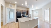 This 1-bedroom, 1-bathroom unit in San Antonio, Texas offers a practical and modern layout designed for comfortable everyday living. The open-concept kitchen and living area serves as the heart of the home, featuring a large granite-topped island with a built-in sink and stylish pendant lighting overhead. Dark espresso cabinetry contrasts beautifully with the light countertops, and the kitchen is equipped with black appliances including a refrigerator, range, and microwave. Light wood-style flooring flows throughout the main living areas, adding warmth and continuity to the space.

The generously sized bedroom is carpeted for comfort and includes a ceiling fan, a window for natural light, and direct access to a walk-in closet outfitted with wire shelving for ample storage. The bathroom features wood-look flooring, a combined tub and shower with striking marble-style tile surround, and walnut-toned cabinetry with granite countertops. A dedicated closet off the hallway provides additional storage. Throughout the unit, neutral tones, recessed lighting, and clean architectural lines create a bright, cohesive ambiance that is both functional and inviting.