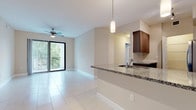 This well-appointed single-floor residence offers a thoughtfully designed open-concept layout that seamlessly connects the kitchen, dining, and living areas. The living space is finished with large, light-reflecting porcelain tile flooring throughout, creating a clean and cohesive aesthetic. A ceiling fan and a full-length sliding glass door lead to a private balcony, framing views of tropical greenery and filling the space with natural light.

The kitchen is a standout feature, showcasing rich dark-toned flat-front cabinetry, granite countertops, and a full suite of stainless steel appliances including a French door refrigerator, electric range, and built-in microwave. A peninsula with a granite overhang and undermount sink serves as both a functional workspace and a casual dining counter. Pendant lighting above the peninsula adds a modern touch, while track lighting illuminates the kitchen workspace. A dedicated laundry area with full-size washer and dryer is conveniently located nearby.

The bedroom is generously sized with large format tile flooring, a walk-in closet, and a window that brings in natural light. The bathroom features large-format tile, a soaking tub with shower, a granite-topped vanity with an undermount sink, and a bright window for ventilation.